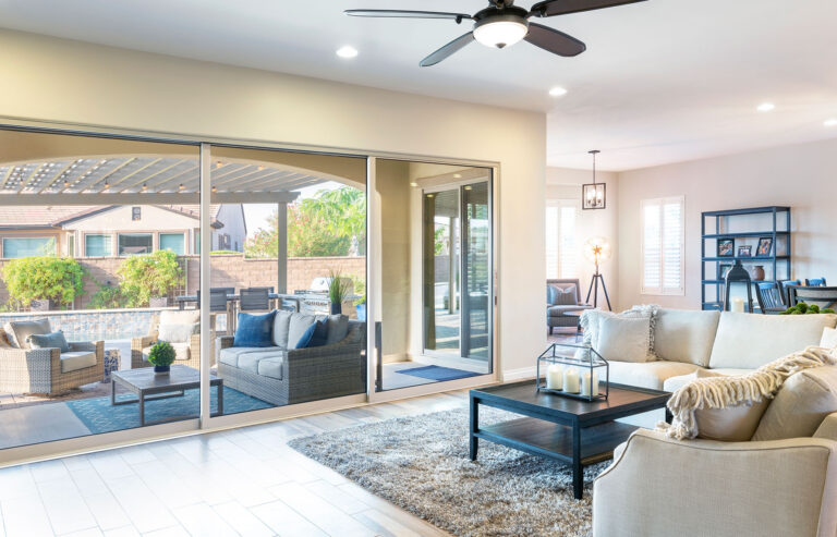 A large sliding glass door connects a living room with a beige couch and shag rug to a covered outdoor seating area.