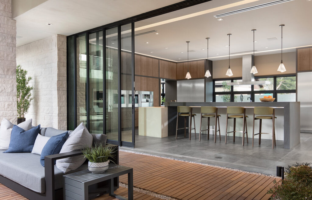 A wall-length open multi-slide glass door connects the outdoor patio to a large kitchen in a farmhouse remodel.
