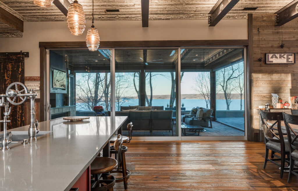 A multi-slide glass door in a rustic lake house kitchen looks onto an enclosed patio with views of a lake.