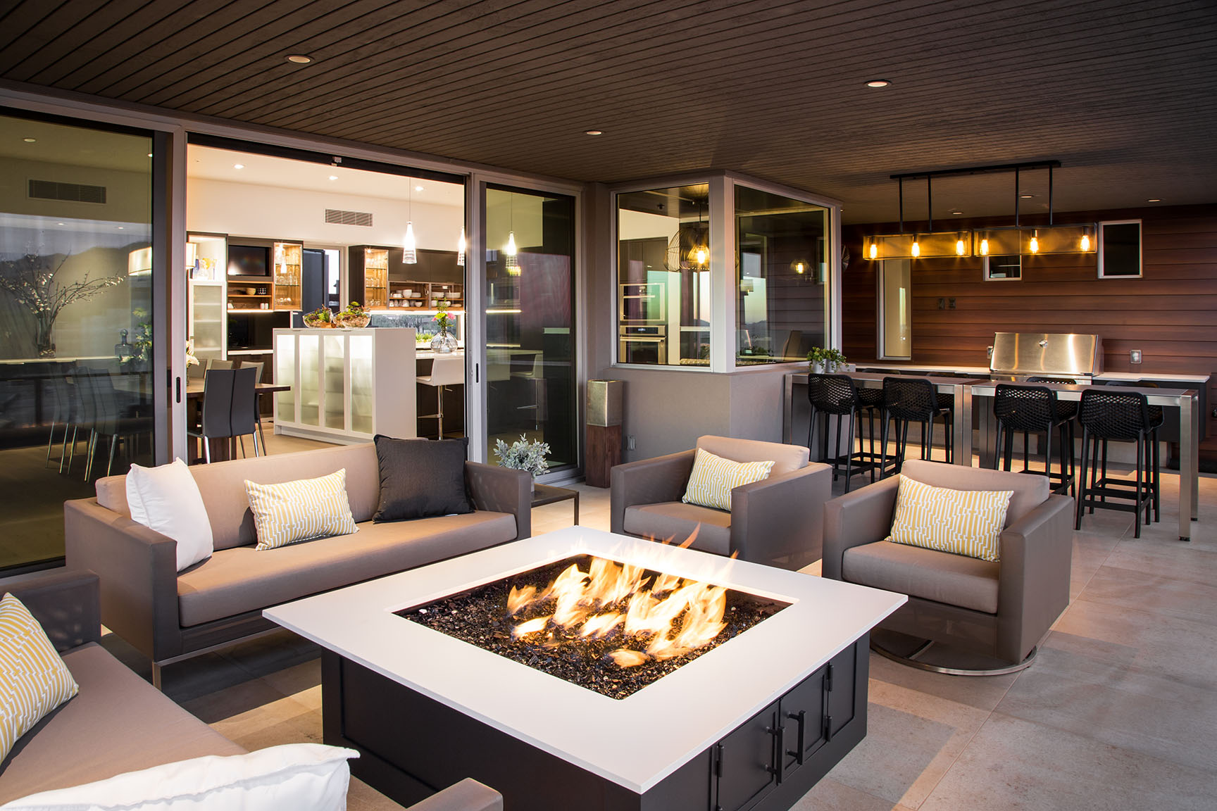 A covered, outdoor seating area with a fire pit in front of a bi-parting, sliding door.