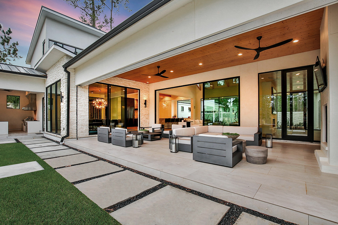 An outdoor entertaining area with two seating areas and an open multi-slide door connecting the space to the living room.