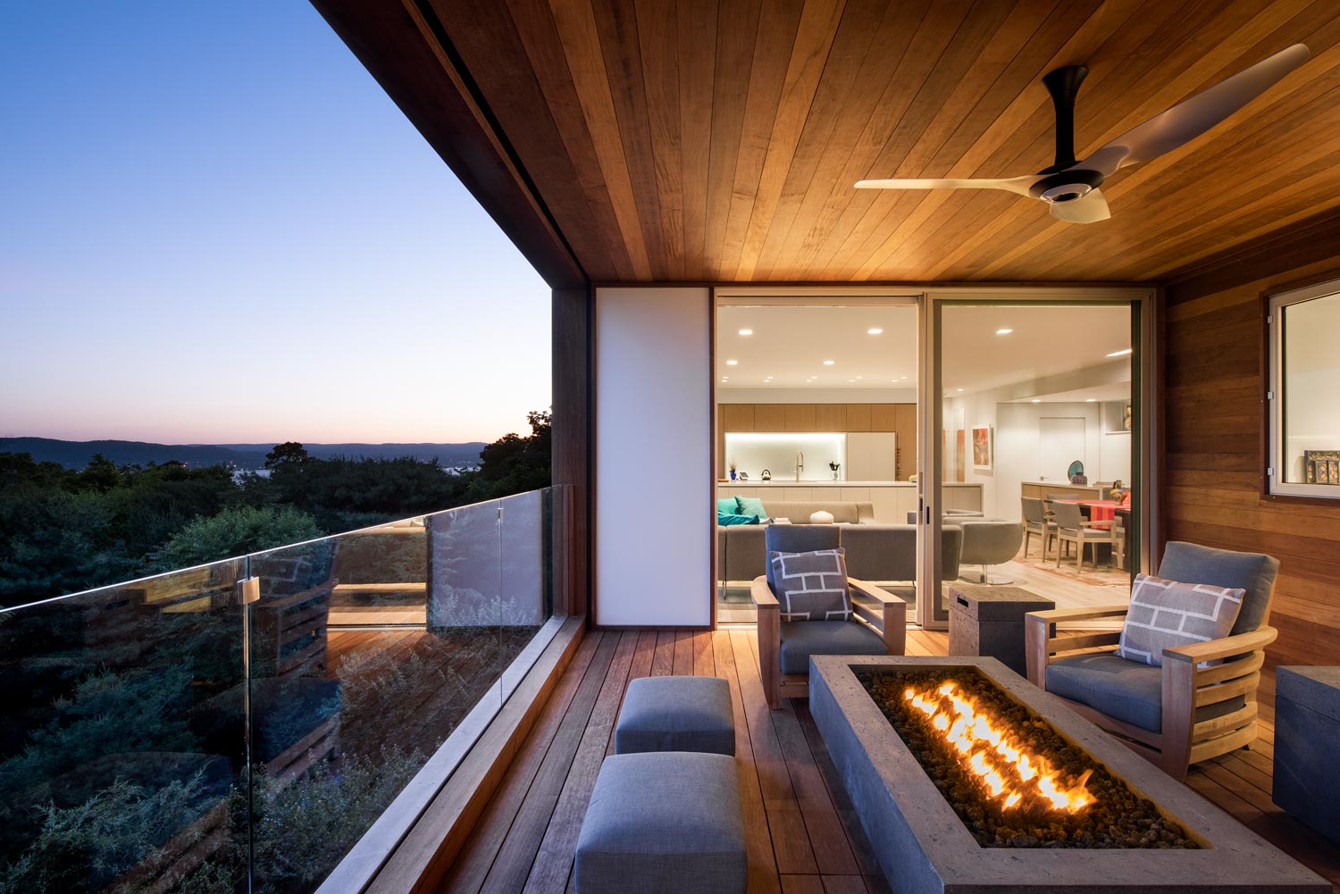 A covered balcony is warmed by a lit fireplace in front of an open sliding door.