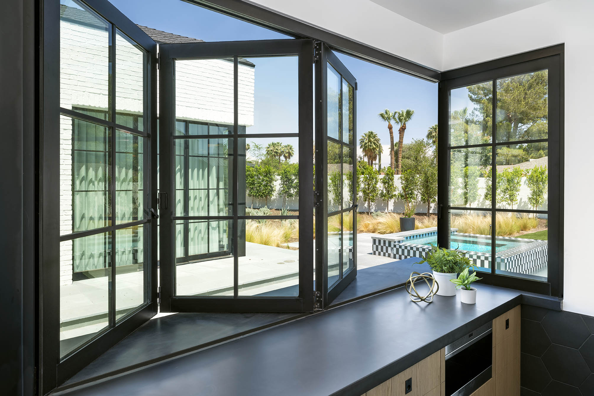 The partly open bi-fold window connects the outdoor pool area to the kitchen.